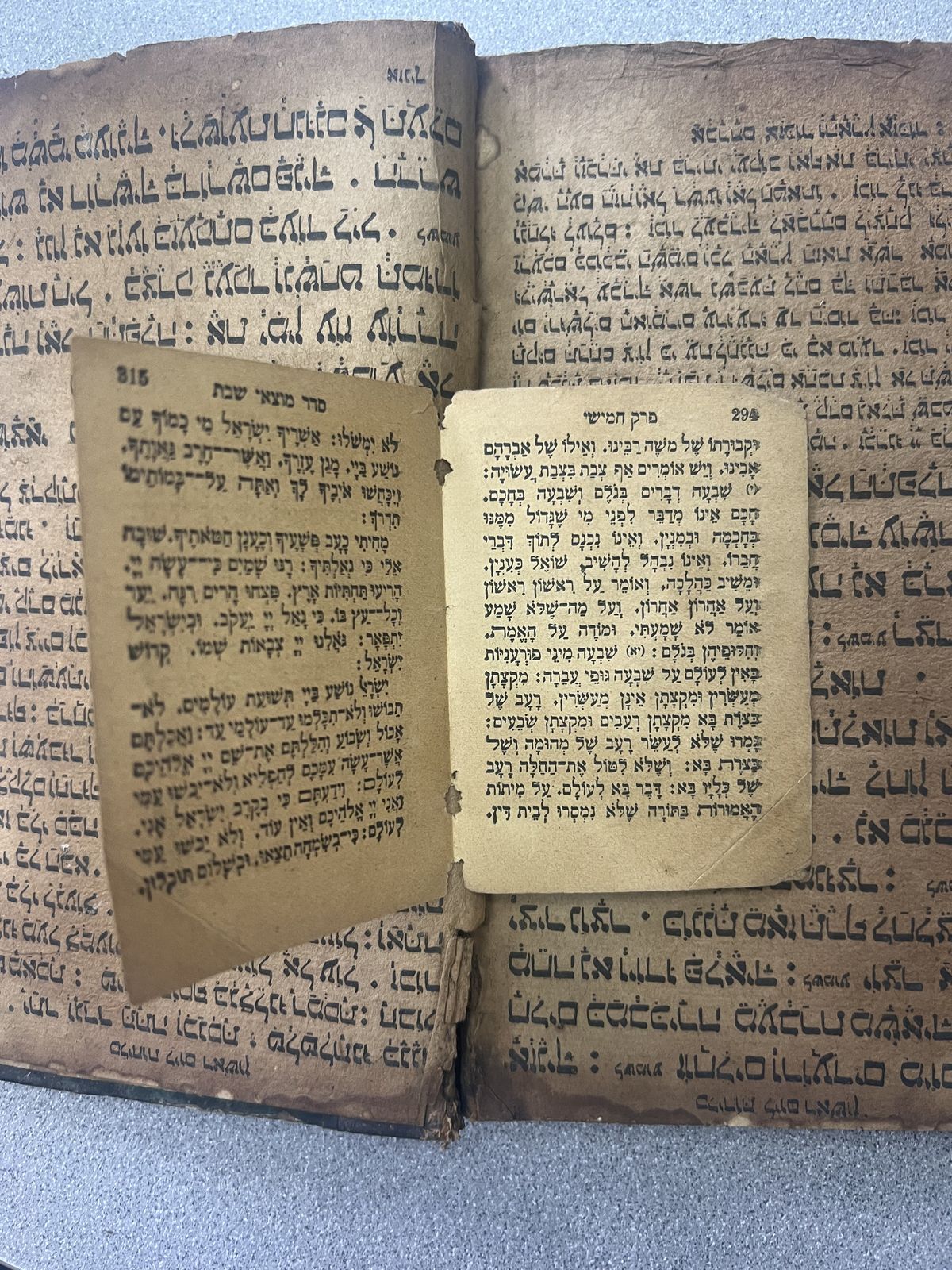Loose printed leaves in square Hebrew type with vowel points, lying on top of the hand-written pages of a different book