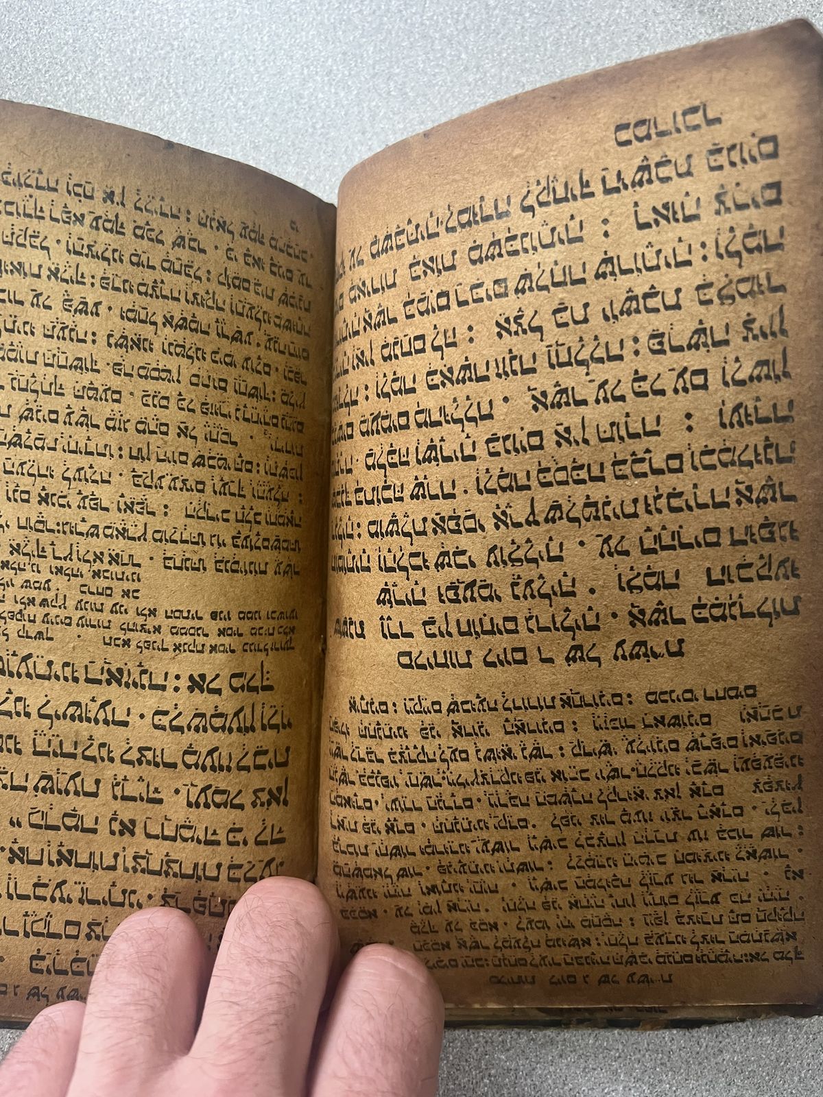 An open hand-written book showing dense right-to-left script in rounded connected letterforms on heavily browned paper
