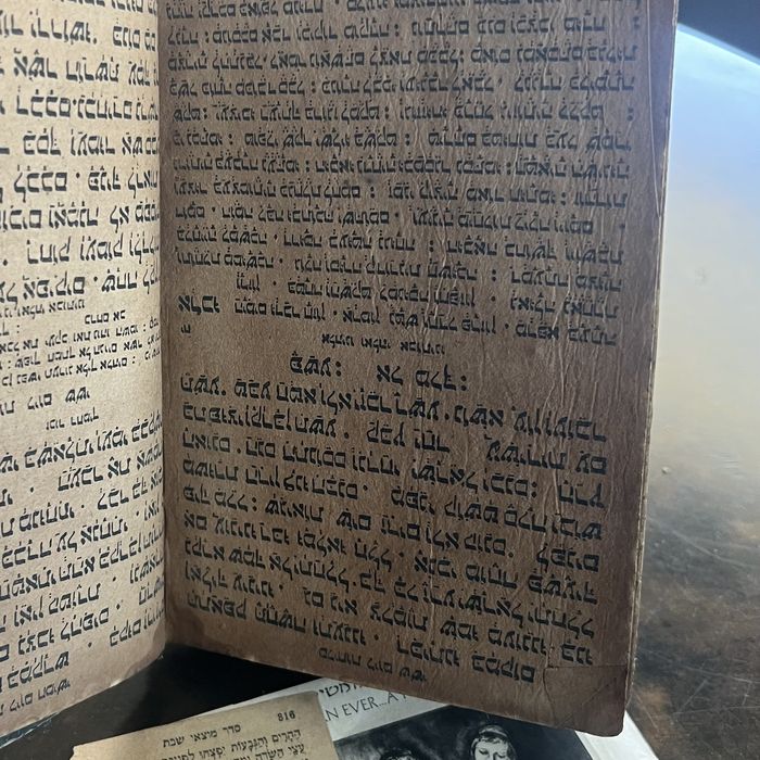 The same book propped open above a printed Hebrew prayer-book leaf and a dealer advertisement