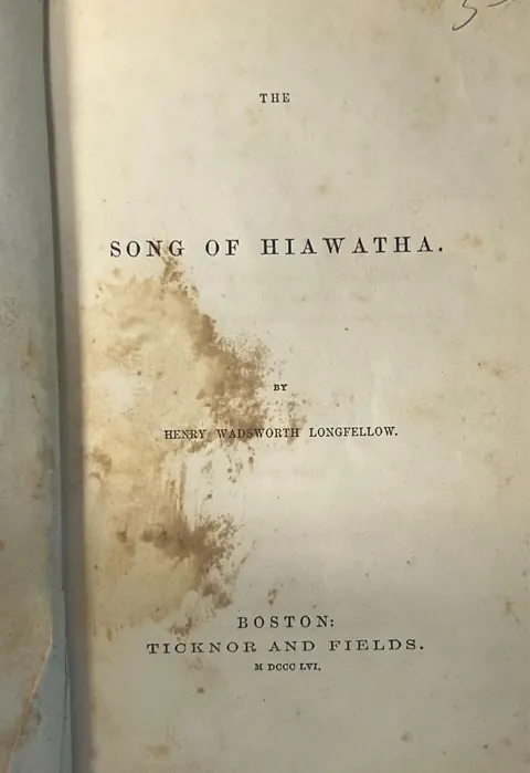 Title page of The Song of Hiawatha, Boston, Ticknor and Fields, MDCCCLVI, with a large brown water stain spreading across the lower half of the page and over the author's name