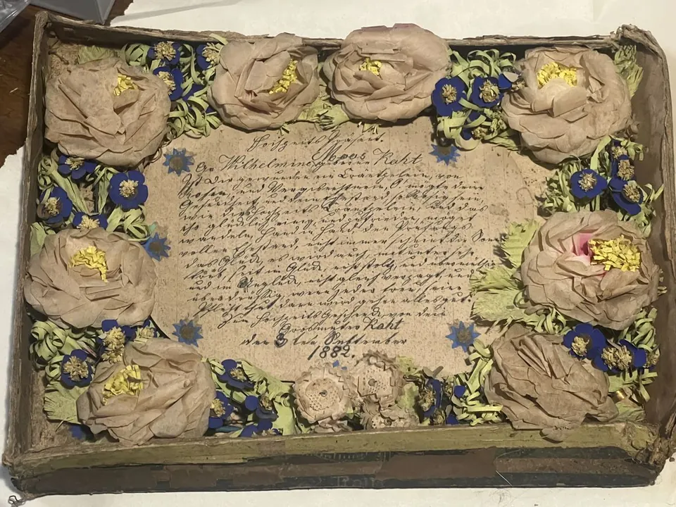 An 1882 handmade paper-flower keepsake under glass in an embossed oval frame