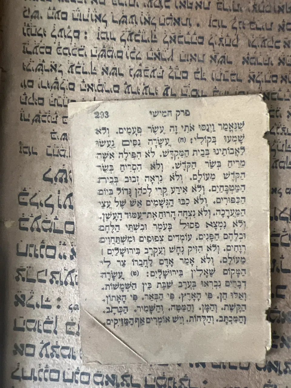 A loose printed Hebrew leaf from Pirkei Avot lying on the open pages of the hand-written Syriac manuscript