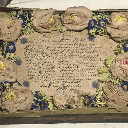 Handmade paper roses and blue paper flowers wreathed around a handwritten German document